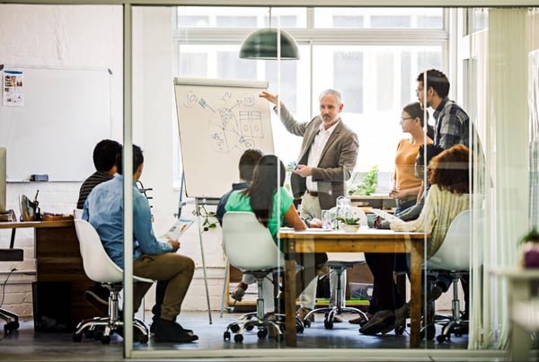 Team meeting around a table and one person drawing a chart